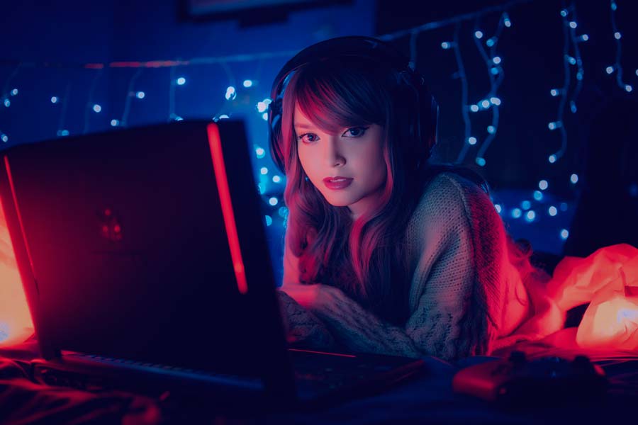 Chica con auriculares gaming tumbada junto a un portátil gaming